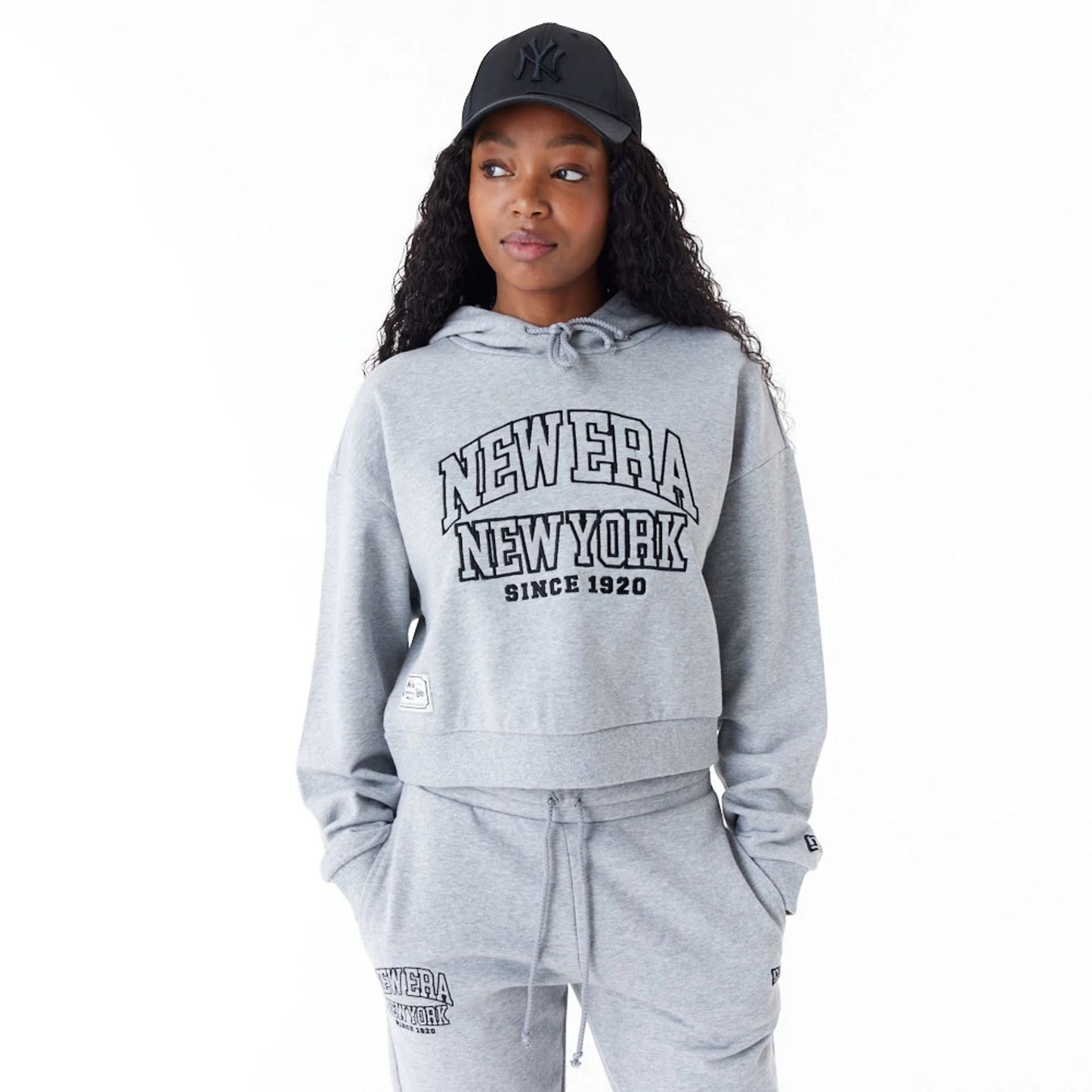 The Female model is wearing New Era Womens Arch Wordmark Grey Crop Pullover Hoodie 1