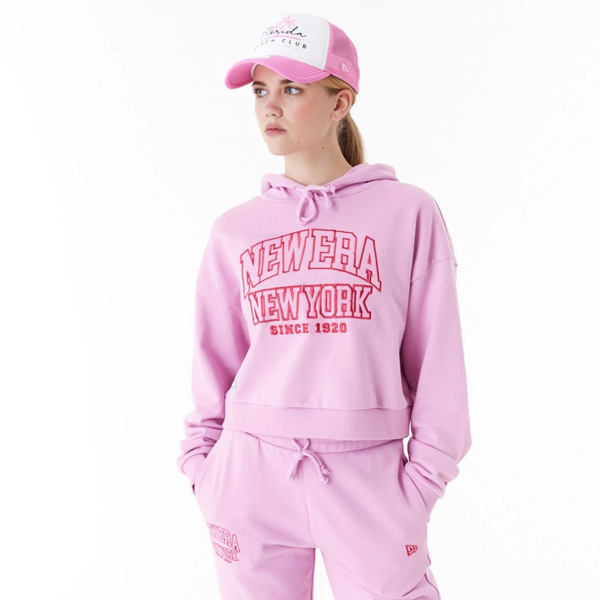 The Female model is wearing New Era Womens Arch Wordmark Pink Crop Pullover Hoodie 1