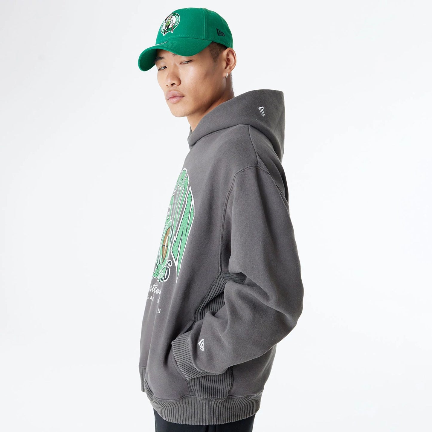 The Male model is wearing Boston Celtics Oversized Essential Dark Grey Oversized Pullover Hoodie 7